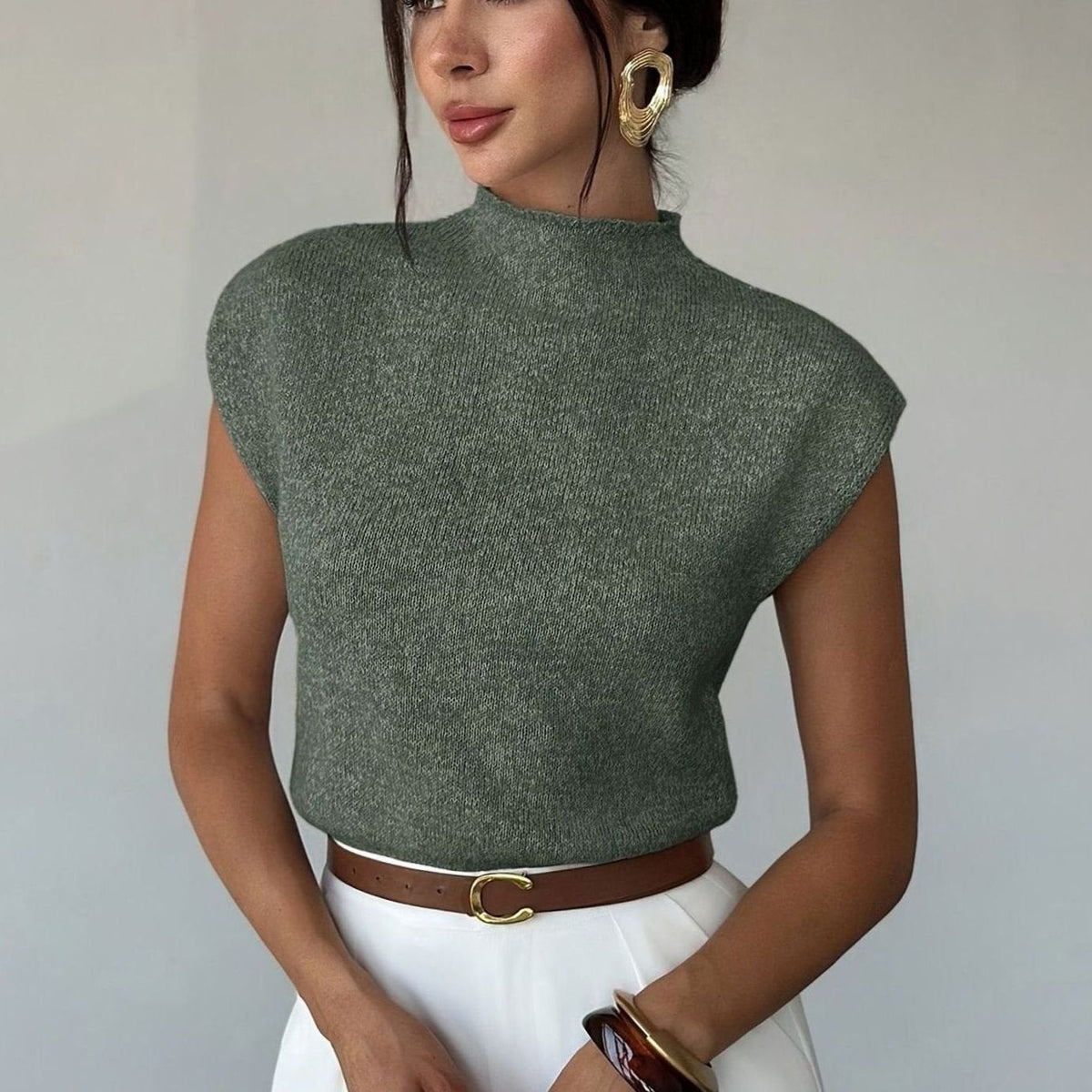 Olijfgroene gebreide damesspencer met opstaande col, gedragen met een witte broek en een bruine riem
