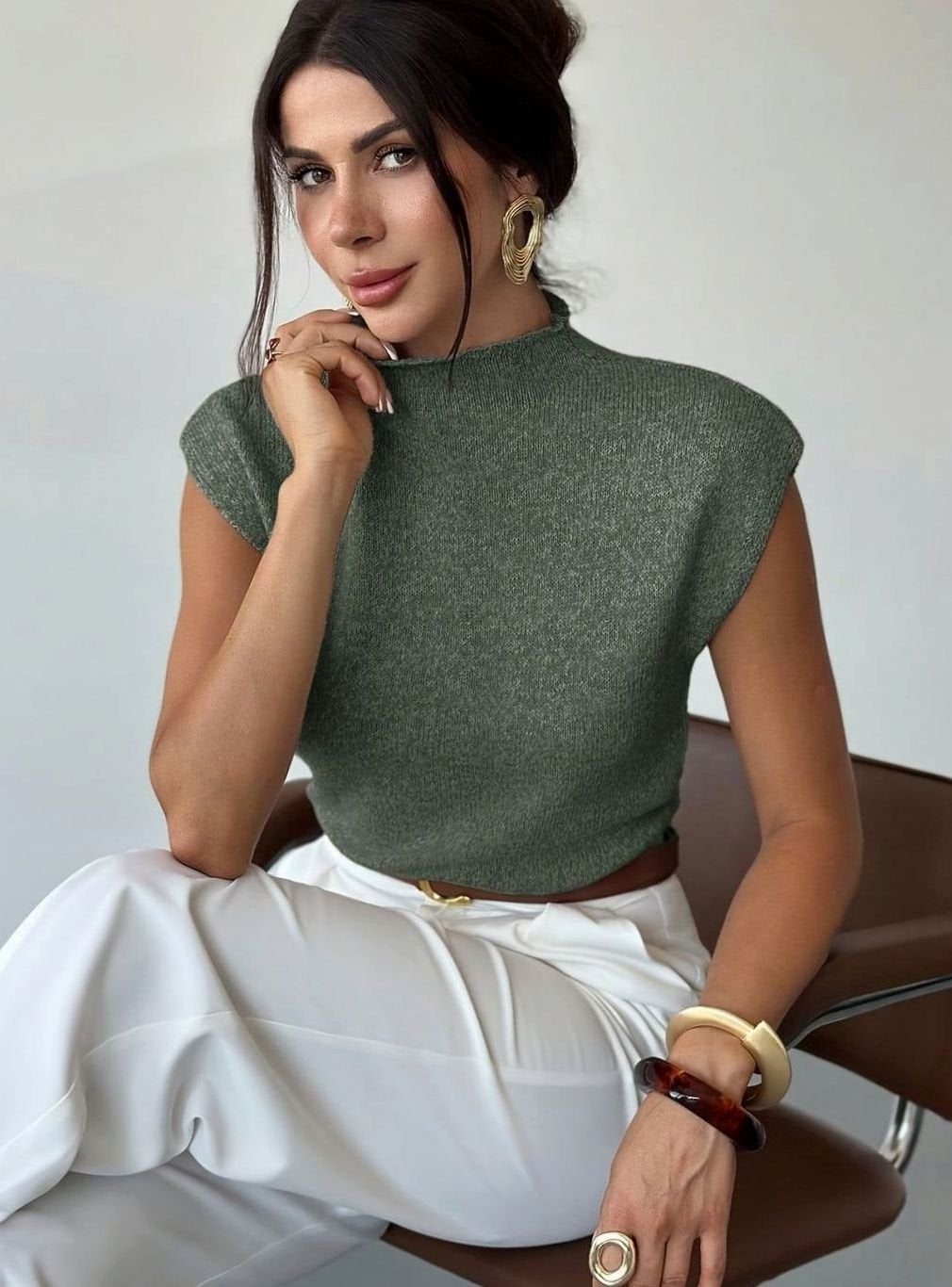 Zittende vrouw in een olijfgroene spencer met opstaande col en een witte broek