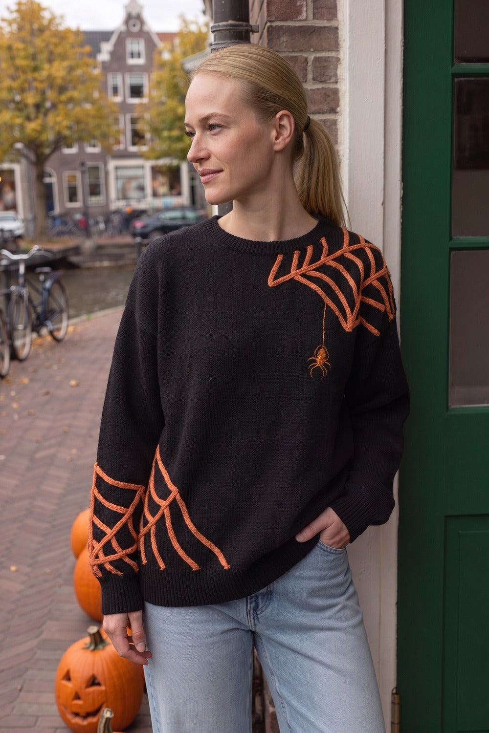 Vrouw in de zwarte spinnenwebtrui met lichtblauwe jeans bij een Amsterdamse grachtenpanddeur