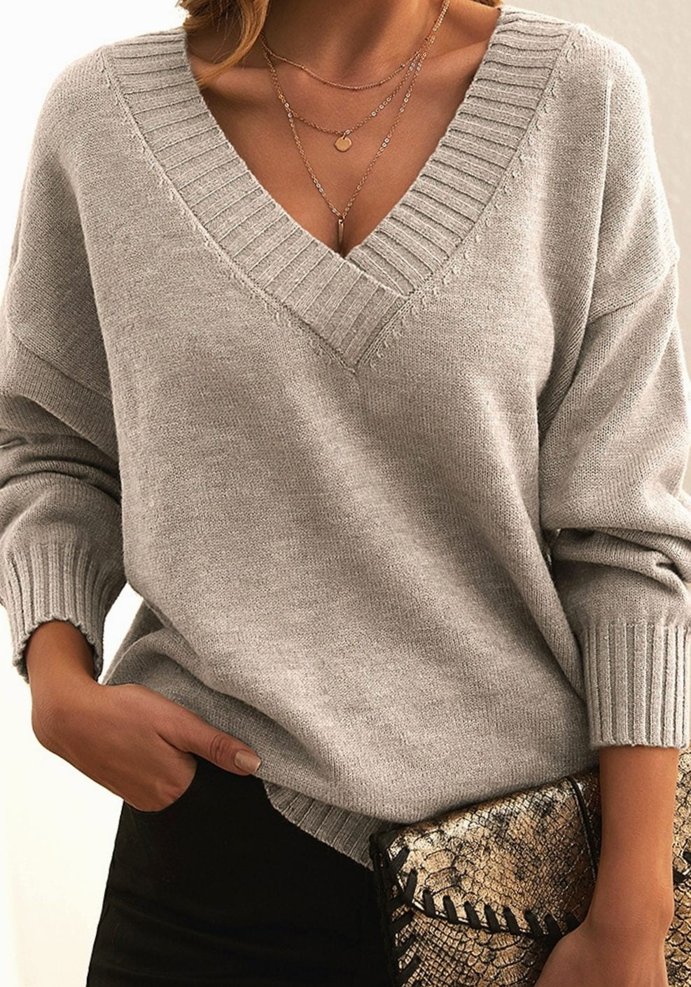 Beige trui met V-hals, gedragen met een zwarte broek en een clutch met slangenprint
